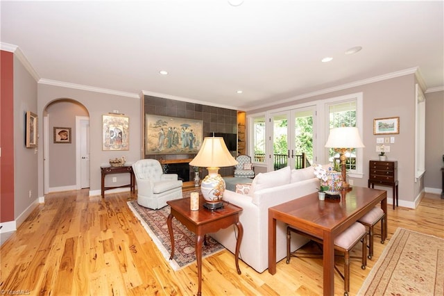 living room with french doors, ornamental molding, a tiled fireplace, and light hardwood / wood-style floors