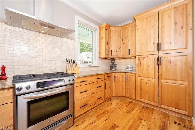 kitchen featuring wall chimney range hood, ornamental molding, light stone countertops, light hardwood / wood-style floors, and gas range