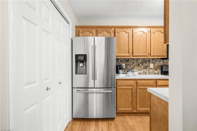 kitchen featuring light wood-type flooring, backsplash, a textured ceiling, and stainless steel fridge with ice dispenser