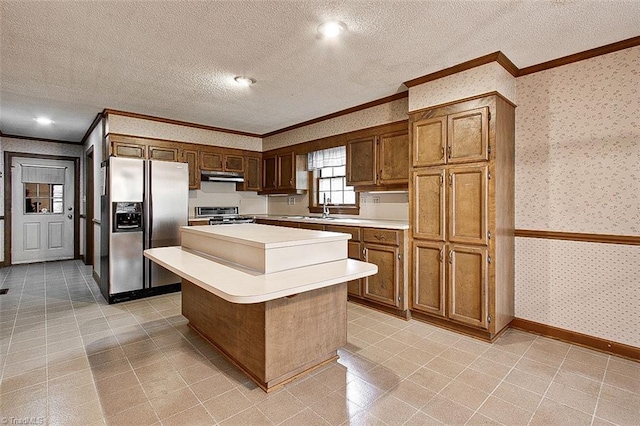 kitchen featuring sink, ornamental molding, a kitchen island, a textured ceiling, and appliances with stainless steel finishes