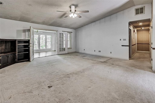 unfurnished living room featuring lofted ceiling, ceiling fan, light colored carpet, and a textured ceiling