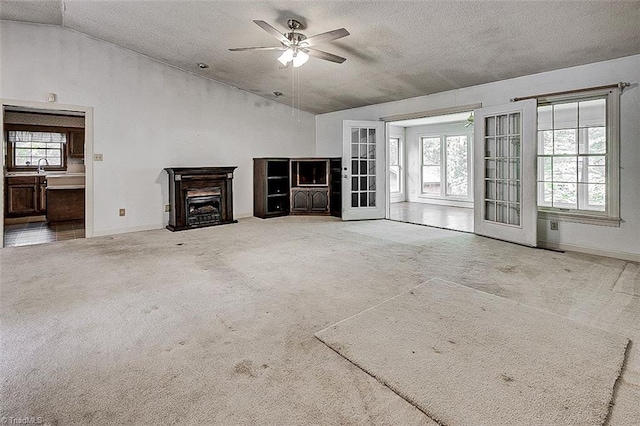 unfurnished living room with ceiling fan, a textured ceiling, lofted ceiling, and a healthy amount of sunlight