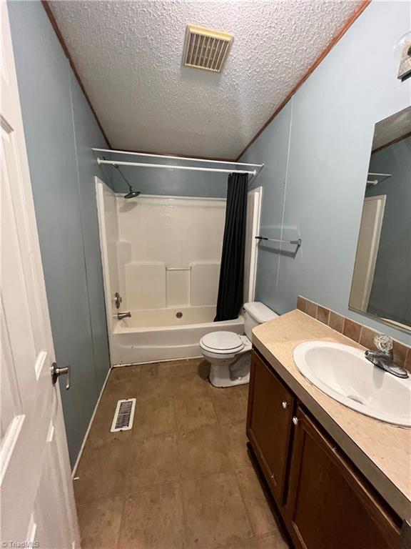 full bathroom with vanity, shower / bath combo, toilet, and a textured ceiling