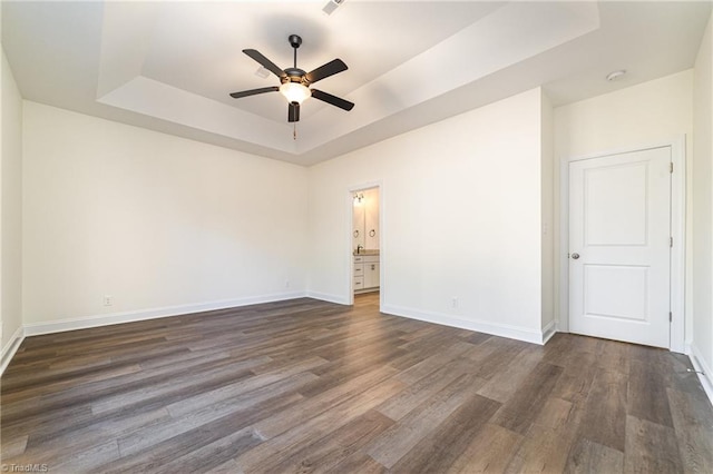 unfurnished room featuring dark wood finished floors, baseboards, a raised ceiling, and a ceiling fan