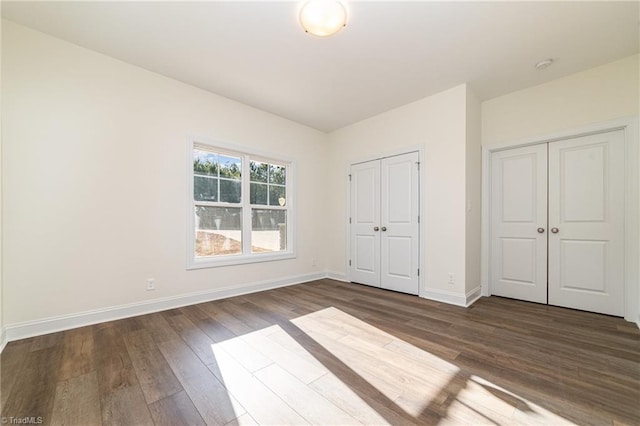 unfurnished bedroom with baseboards, two closets, and dark wood finished floors