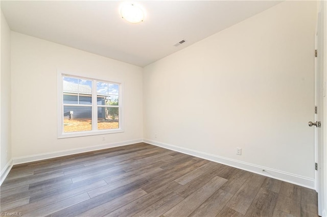spare room with dark wood-style floors, visible vents, and baseboards
