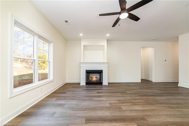 unfurnished living room with visible vents, recessed lighting, a warm lit fireplace, wood finished floors, and a ceiling fan