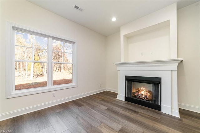 unfurnished living room with visible vents, baseboards, a lit fireplace, and wood finished floors