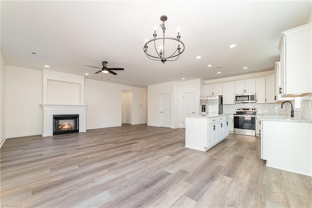 kitchen featuring white cabinets, appliances with stainless steel finishes, ceiling fan with notable chandelier, open floor plan, and a center island