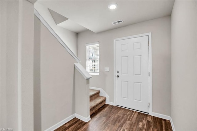 foyer entrance with visible vents, baseboards, dark wood-style floors, and stairway