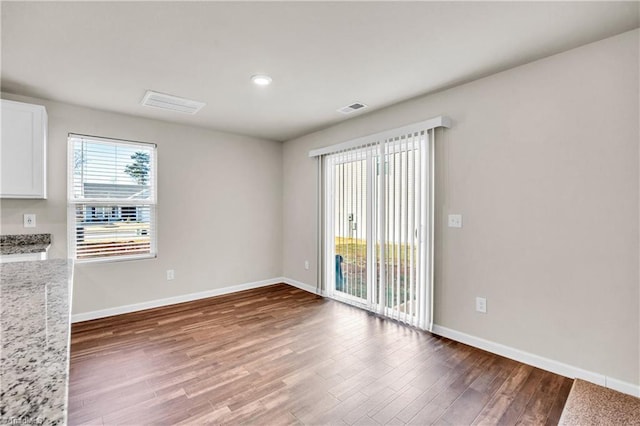 empty room with wood finished floors, visible vents, and baseboards