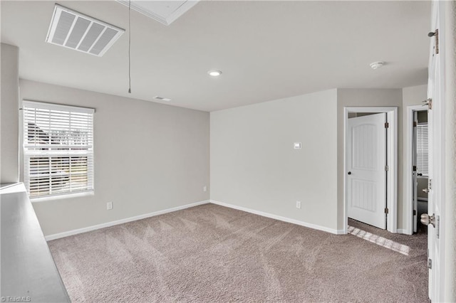 carpeted empty room with visible vents, baseboards, and attic access