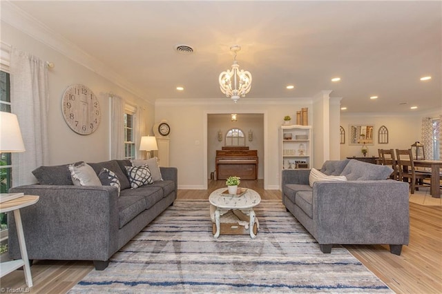 living room featuring an inviting chandelier, light wood-type flooring, crown molding, and ornate columns