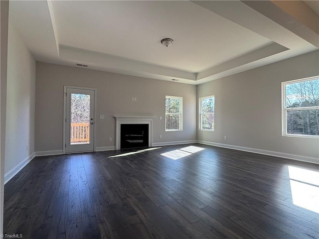 unfurnished living room featuring a wealth of natural light, a tray ceiling, and dark wood finished floors