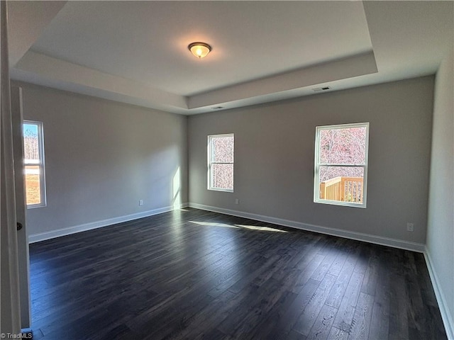 unfurnished room with a tray ceiling, baseboards, and dark wood-type flooring