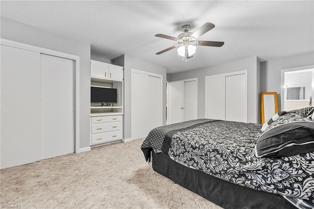 bedroom featuring light carpet, a textured ceiling, two closets, and ceiling fan