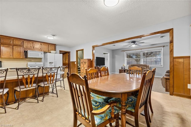 dining space featuring ceiling fan, wood walls, and a textured ceiling