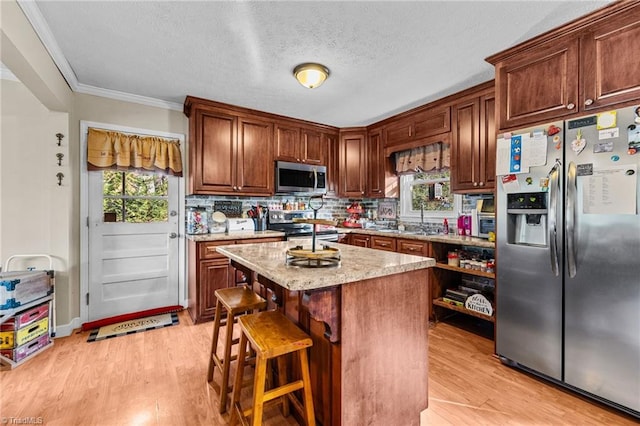 kitchen featuring a wealth of natural light, light stone countertops, a kitchen bar, a kitchen island, and appliances with stainless steel finishes