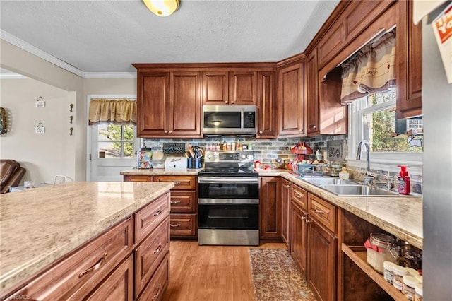 kitchen with ornamental molding, a textured ceiling, stainless steel appliances, sink, and light hardwood / wood-style flooring