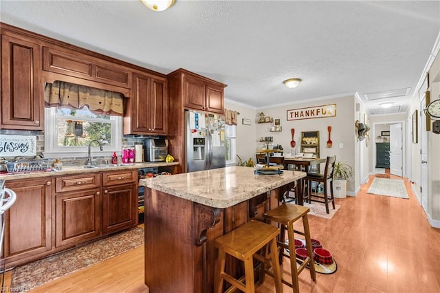 kitchen with a center island, stainless steel fridge with ice dispenser, crown molding, a breakfast bar area, and light wood-type flooring