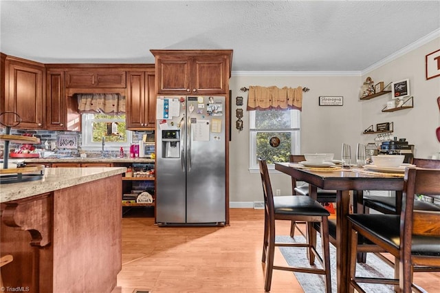 kitchen featuring light stone countertops, stainless steel fridge, plenty of natural light, light hardwood / wood-style floors, and ornamental molding