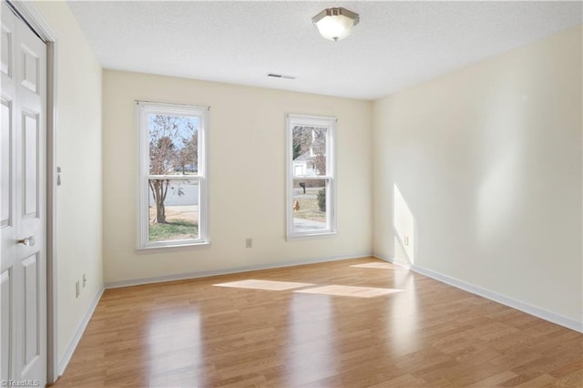 empty room with light wood-type flooring and a textured ceiling