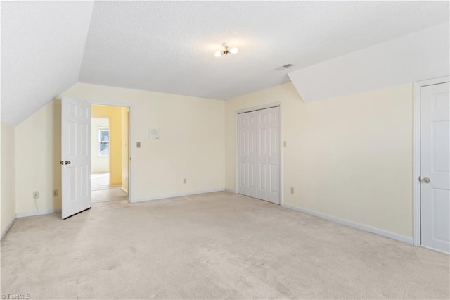 additional living space featuring a textured ceiling, light carpet, and lofted ceiling