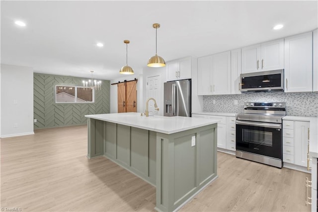 kitchen with white cabinets, light wood finished floors, a barn door, and stainless steel appliances