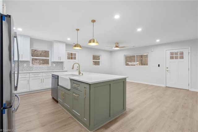 kitchen with stainless steel appliances, light wood-type flooring, white cabinetry, green cabinets, and a sink