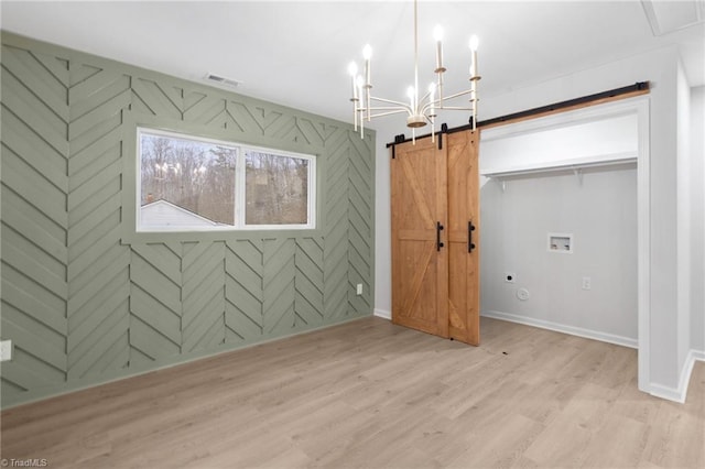 unfurnished bedroom featuring a barn door, a notable chandelier, wood finished floors, visible vents, and baseboards