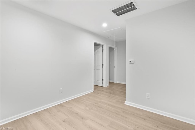 empty room with attic access, visible vents, light wood-style flooring, and baseboards