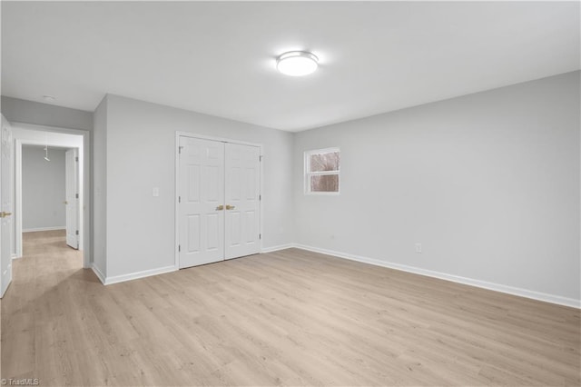 unfurnished bedroom featuring light wood-style flooring, attic access, baseboards, and a closet