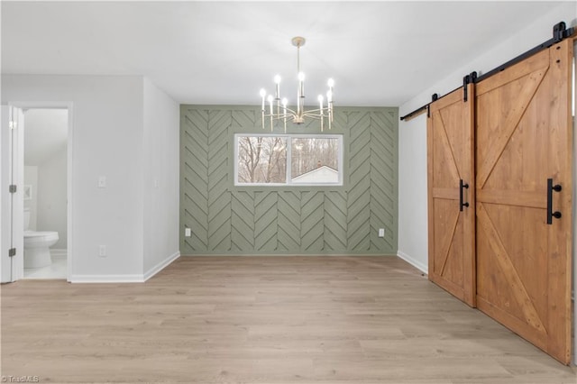 unfurnished dining area featuring a barn door, baseboards, light wood-style flooring, and a notable chandelier