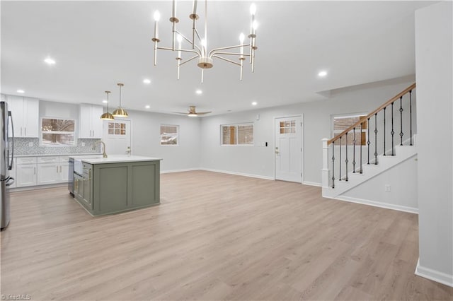 kitchen featuring a kitchen island with sink, light wood-style flooring, white cabinetry, freestanding refrigerator, and decorative backsplash