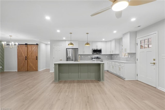 kitchen with a barn door, stainless steel appliances, white cabinets, light countertops, and decorative backsplash