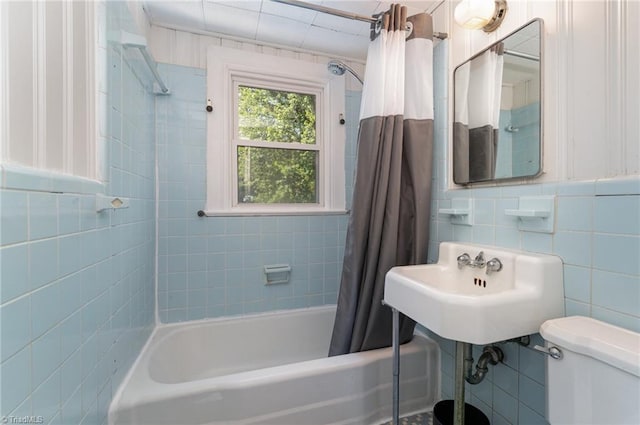 bathroom with tile walls, shower / bath combo with shower curtain, and toilet