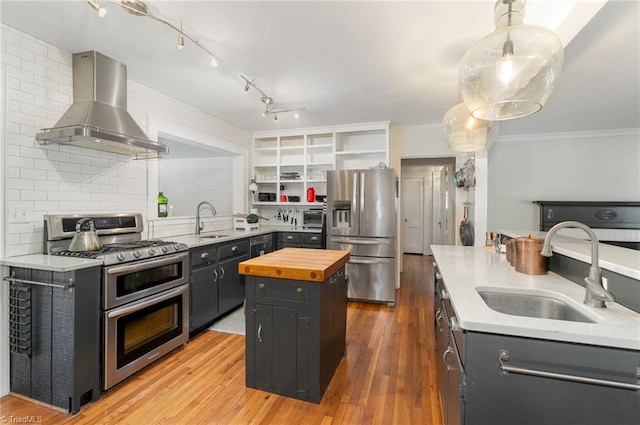 kitchen with sink, wall chimney range hood, stainless steel appliances, a center island, and decorative light fixtures