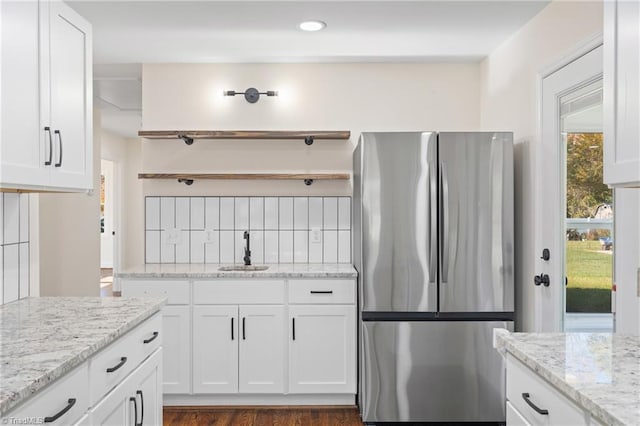 kitchen with white cabinets, stainless steel fridge, light stone countertops, and sink