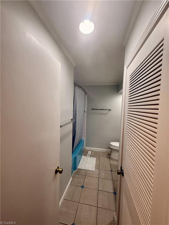 bathroom with toilet, tile patterned floors, ornamental molding, and shower / bath combo with shower curtain