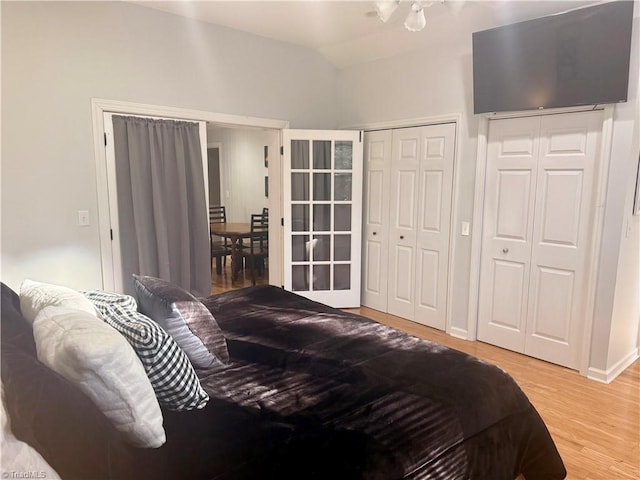 bedroom with two closets, light hardwood / wood-style flooring, and lofted ceiling