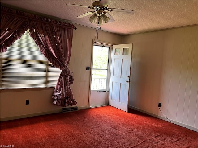 carpeted empty room featuring a textured ceiling, ceiling fan, baseboards, and wood walls