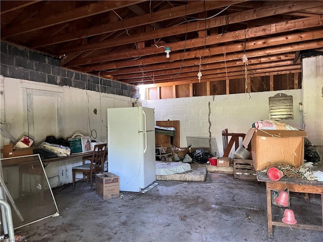 unfinished basement featuring freestanding refrigerator and concrete block wall