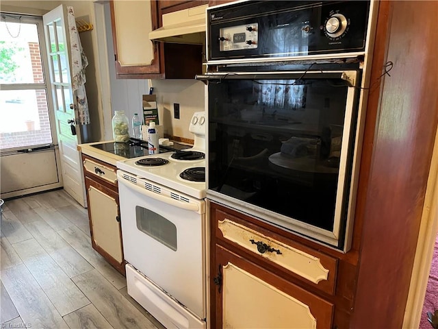 kitchen with white electric stove, oven, under cabinet range hood, light countertops, and light wood finished floors