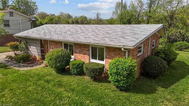 view of property exterior featuring roof with shingles, brick siding, a yard, and an attached garage