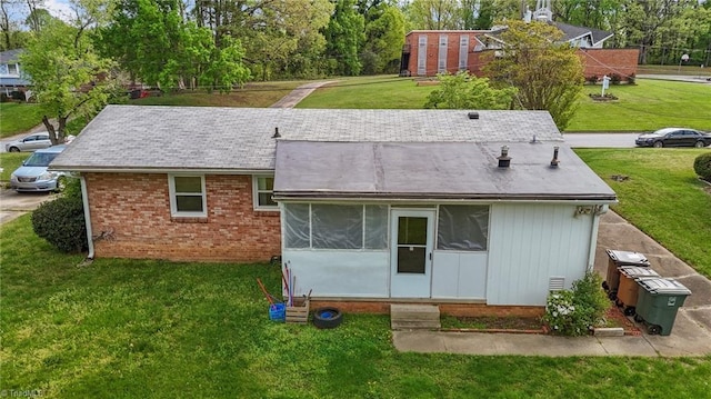 back of property featuring a lawn and brick siding