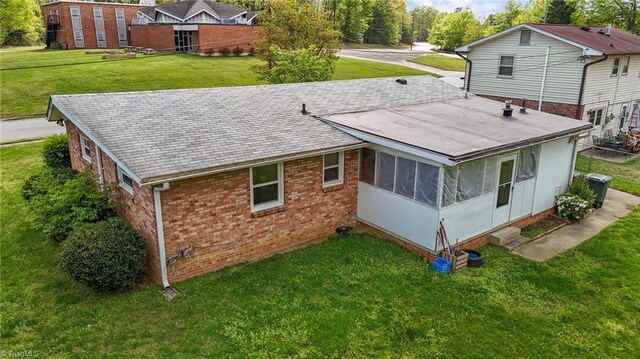 back of house featuring brick siding, a yard, and a sunroom