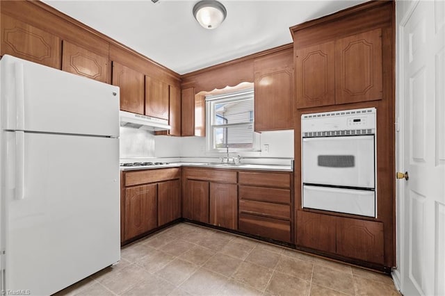 kitchen with brown cabinets, under cabinet range hood, light countertops, white appliances, and a warming drawer