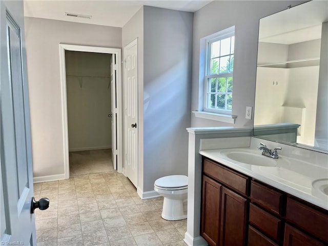 bathroom with a sink, double vanity, toilet, baseboards, and visible vents