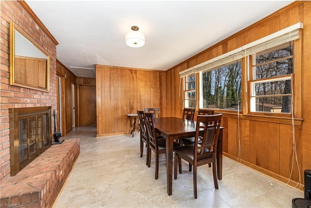 dining space with a brick fireplace, wood walls, and ornamental molding