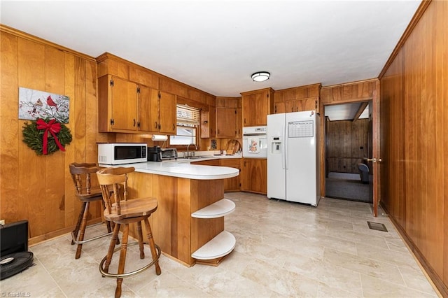 kitchen featuring white appliances, kitchen peninsula, wood walls, a kitchen bar, and sink